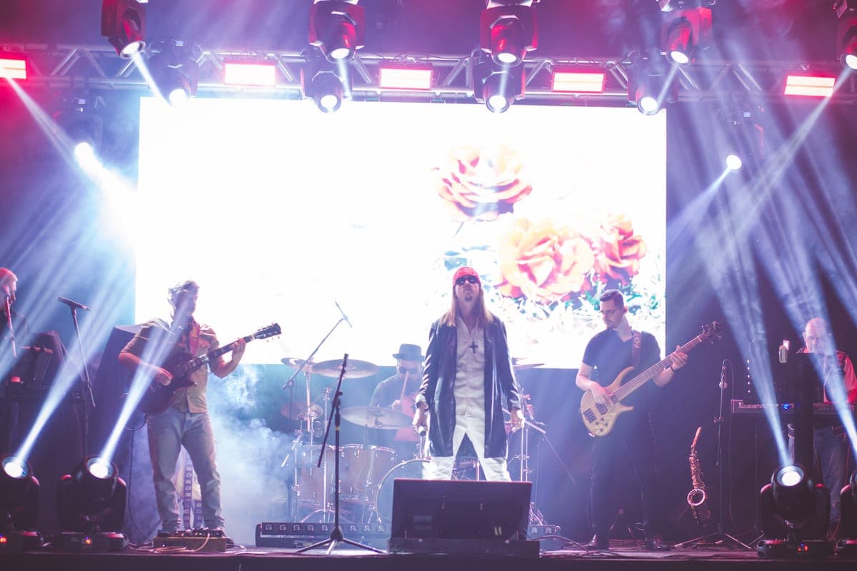 Banda completa no palco sob feixes de luz robotizada e telão de LED