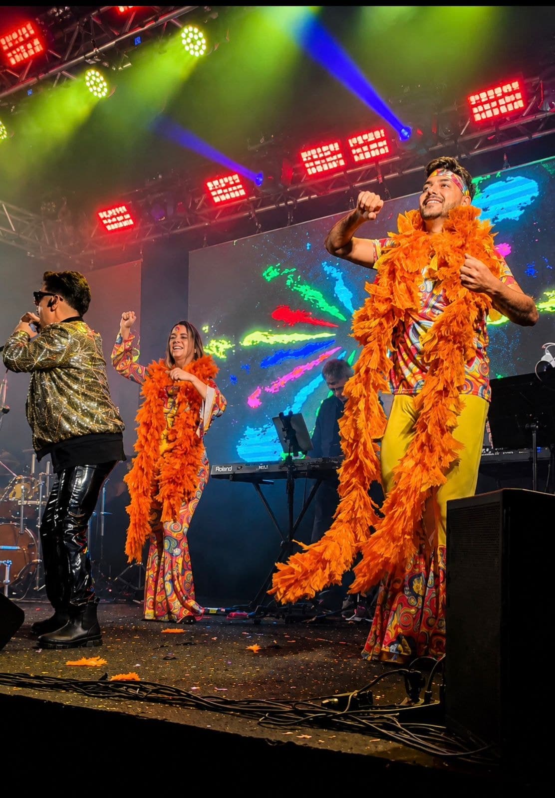 Bloco anos 70 com plumas laranja diante do painel de LED